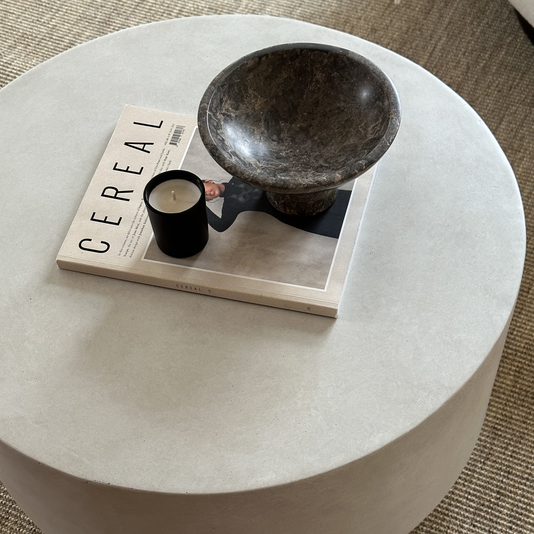Minimalist concrete round coffee table adorned with book, candle, and bowl
