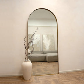 Full length arched gold extra large metal mirror leaning against wall