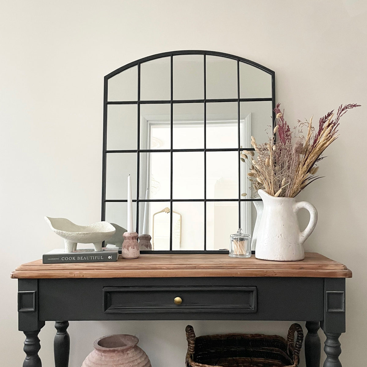 Black industrial arched metal window mirror displayed on console table
