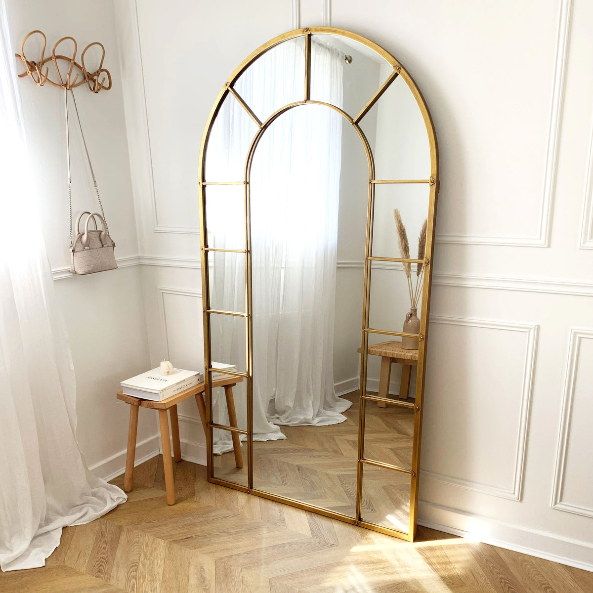 Gold industrial arched full length metal mirror leaning against wall