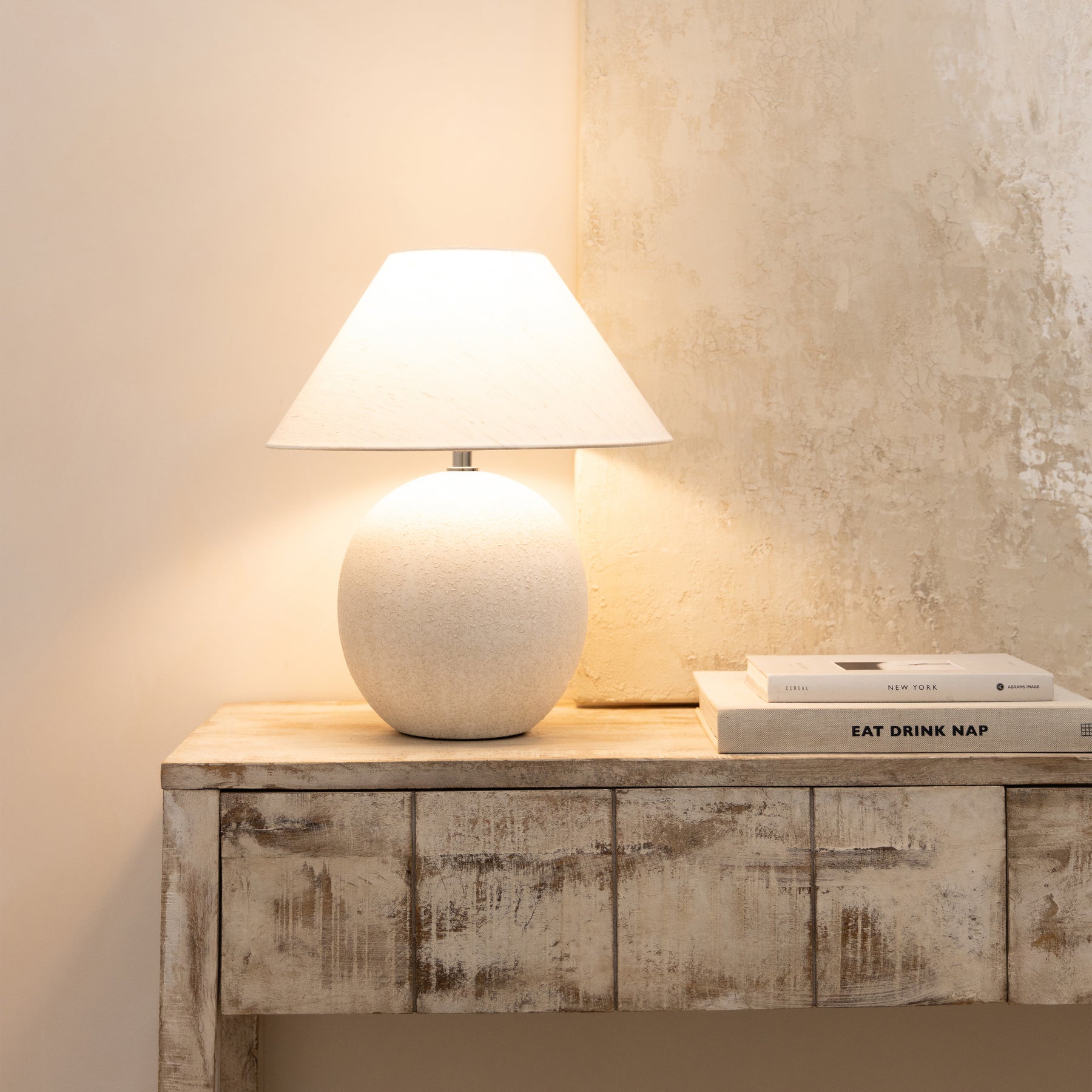 Stone ceramic coolie shade table lamp on console table emitting warm lighting