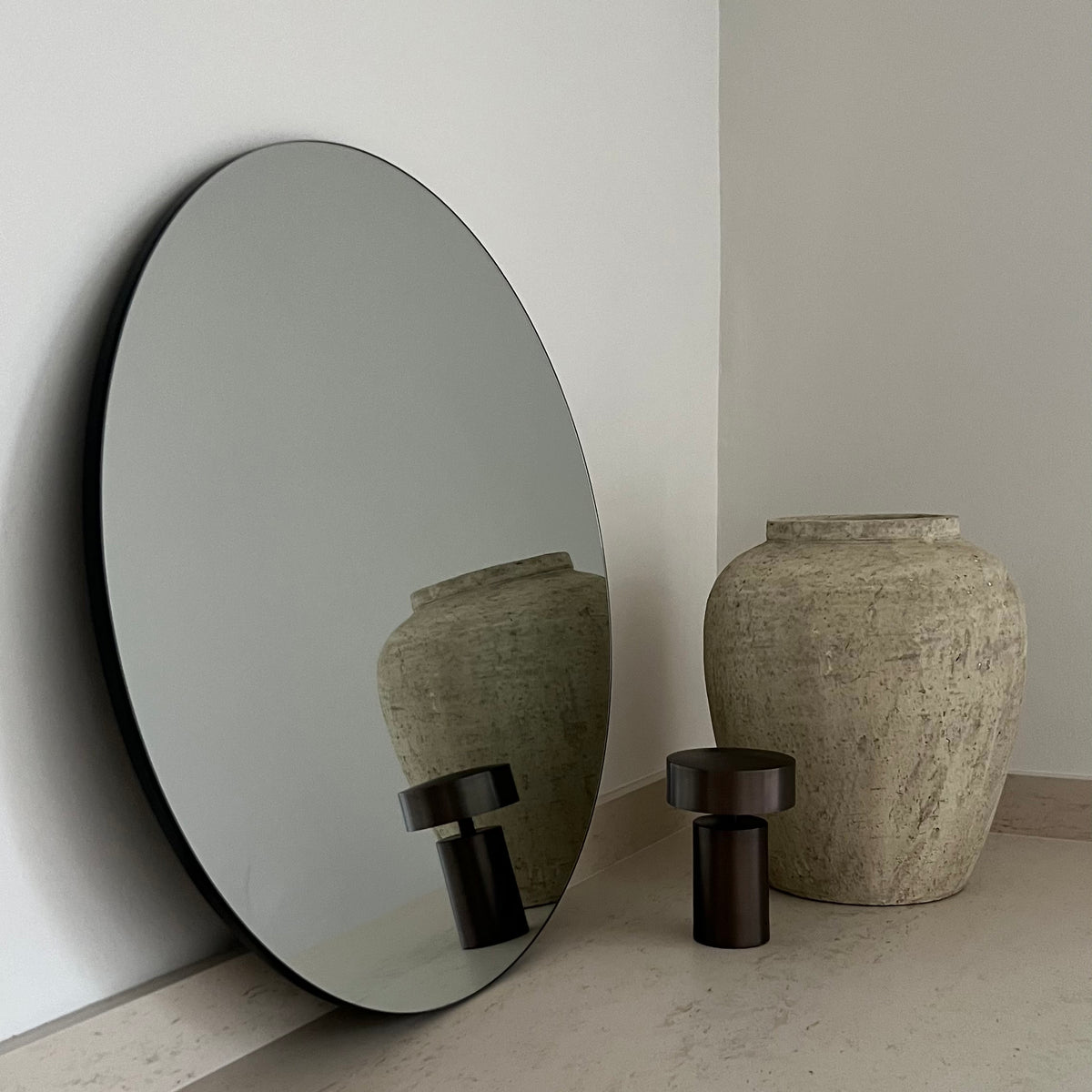 Small Frameless Round Wall Mirror leaning against wall, adjacent to vase