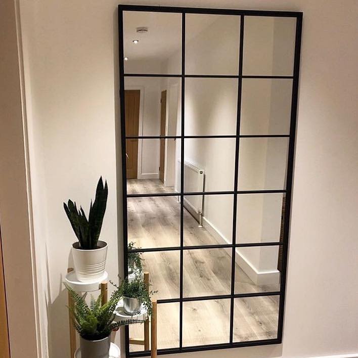 Full length large black metal window mirror functioning as a wall mirror beside plants