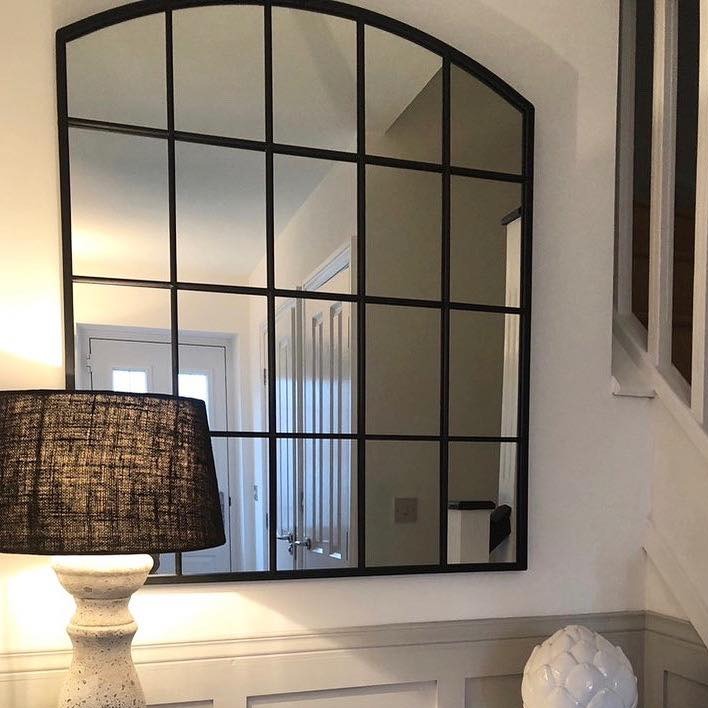 Black industrial arched metal window mirror displayed on wall with warm lighting