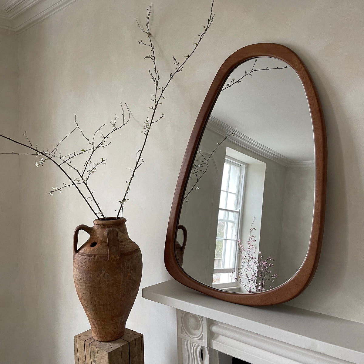 Organic irregular walnut-coloured wooden wall mirror leaning against wall