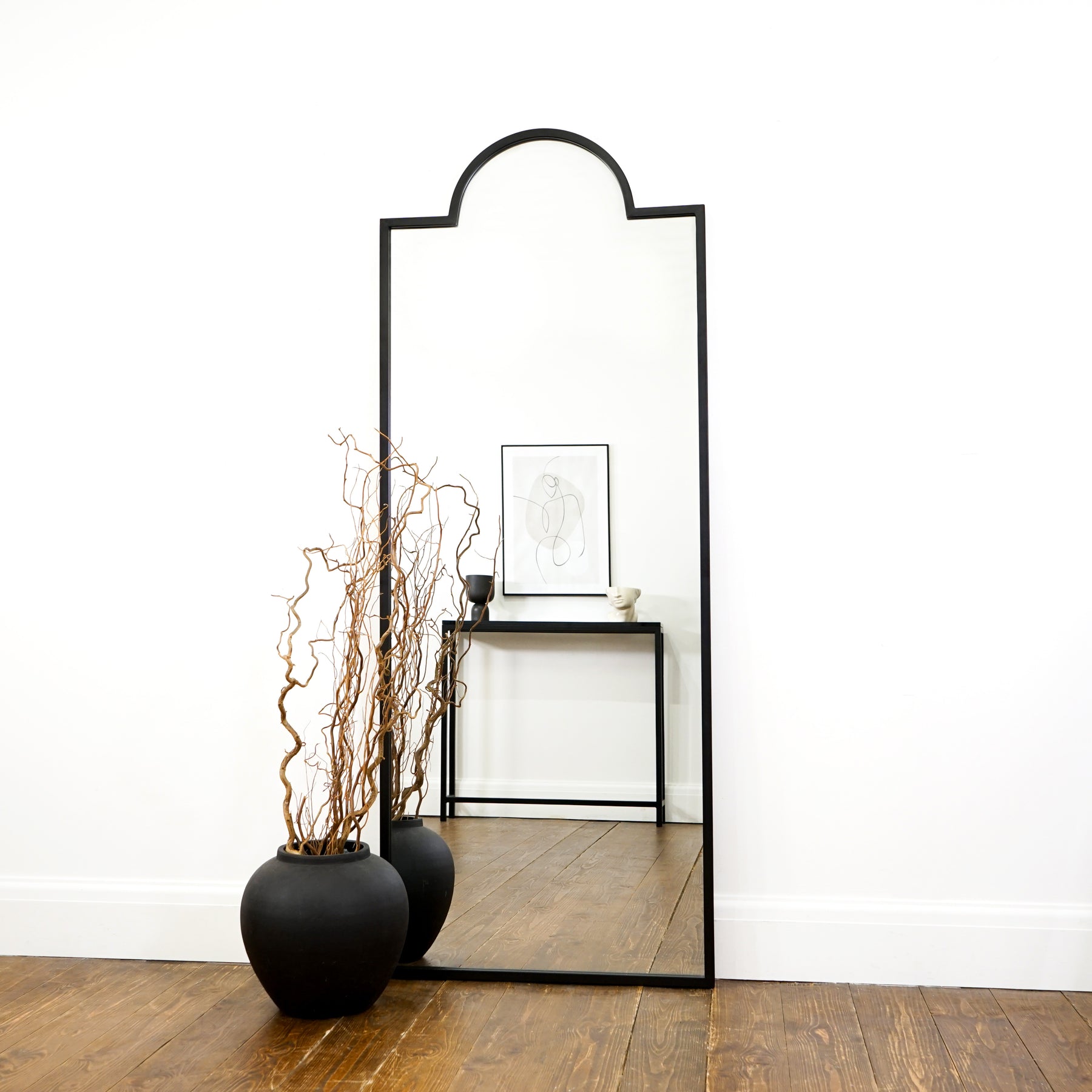 Full length black industrial arched metal mirror beside vase