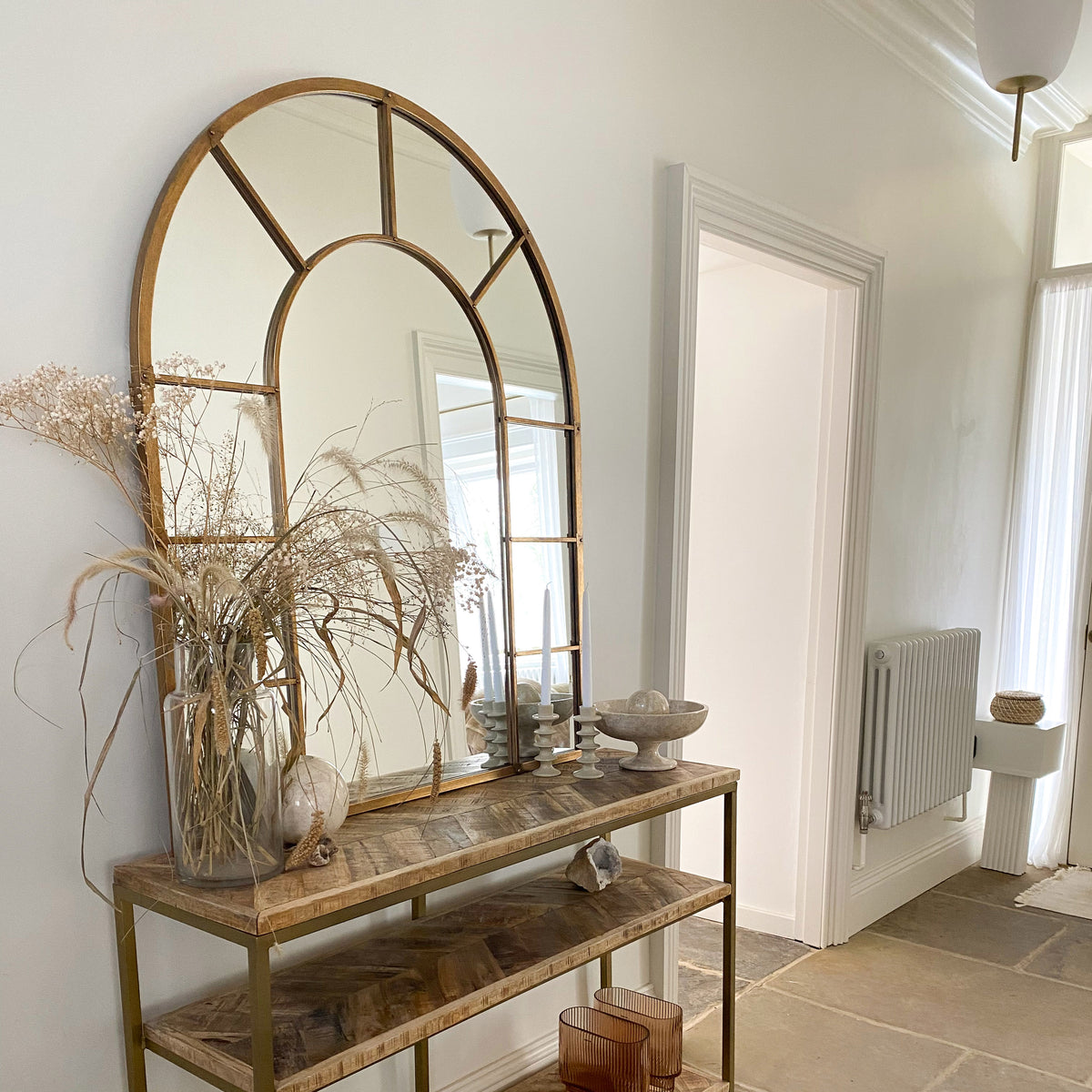 Gold industrial arched metal wall mirror on wooden console table