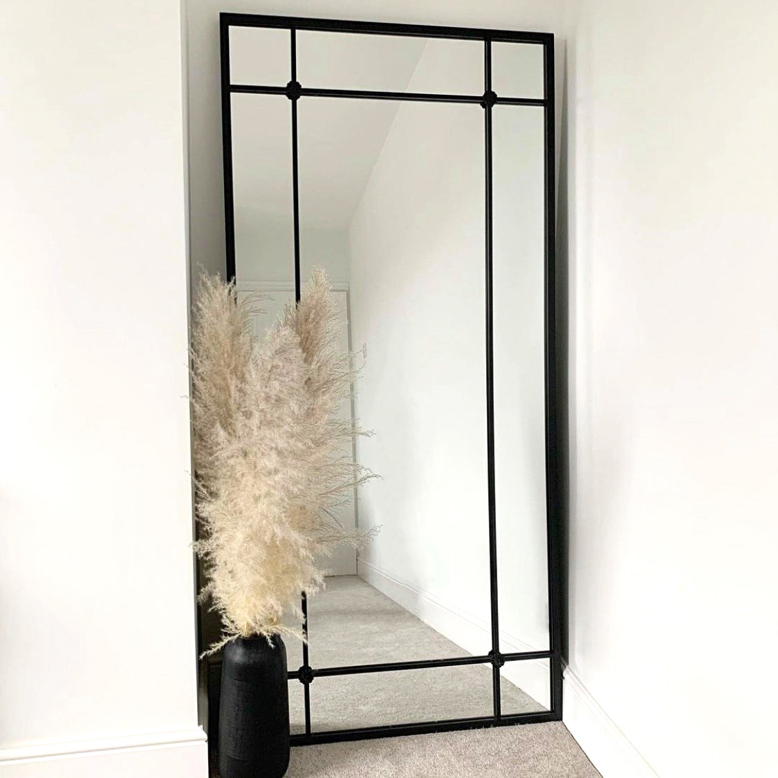 Black industrial full length metal mirror beside vase
