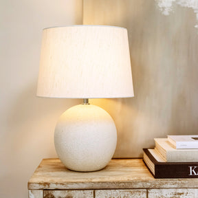 Stone ceramic drum shade table lamp emitting warm light on console table