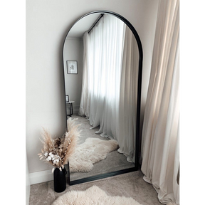 Full length arched black large metal mirror leaning against wall