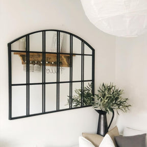 Black industrial arched metal window mirror displayed on wall