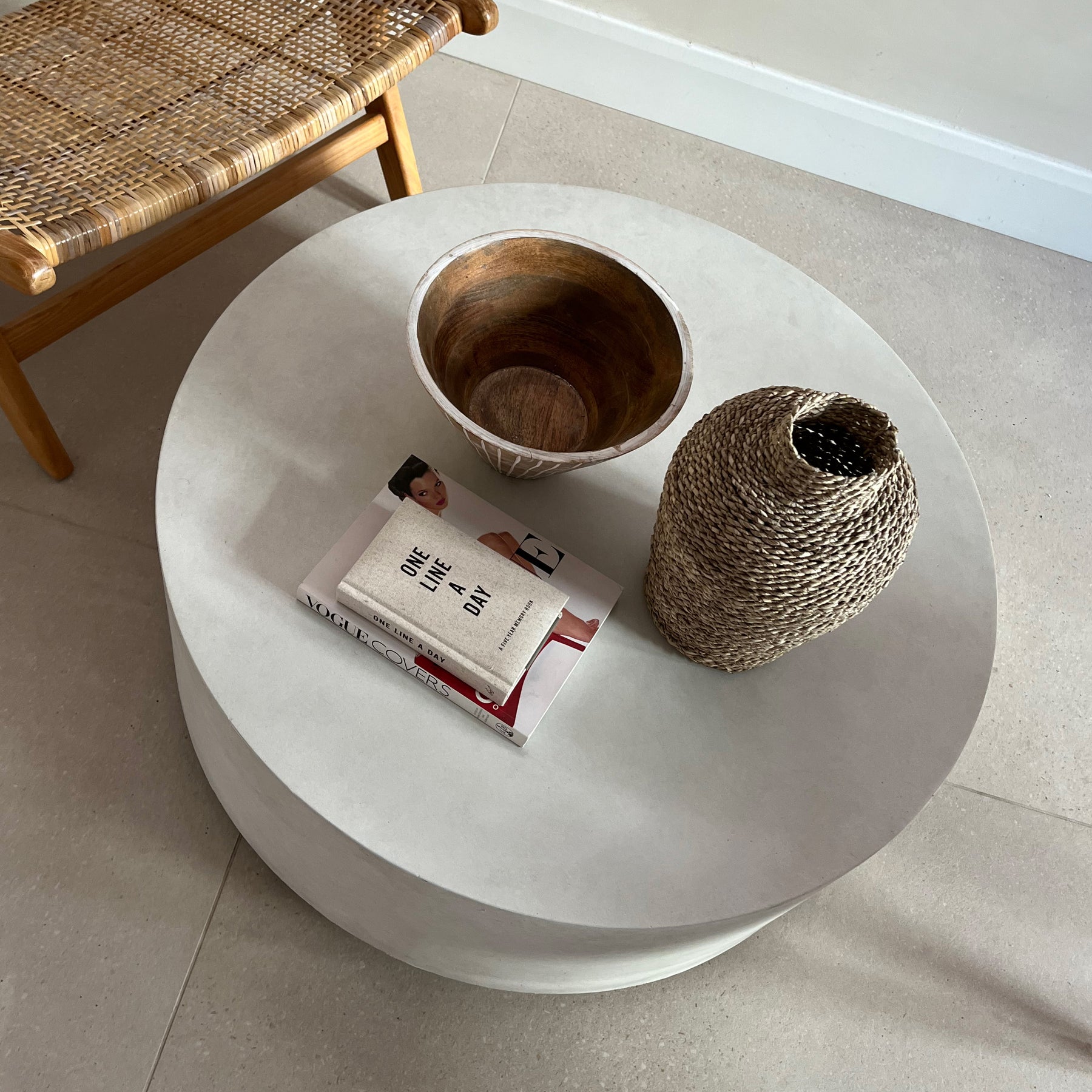 Large minimalist concrete round coffee table adorned with books, basket, and bowl