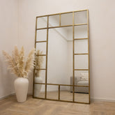 Gold industrial full length metal window mirror leaning against wall