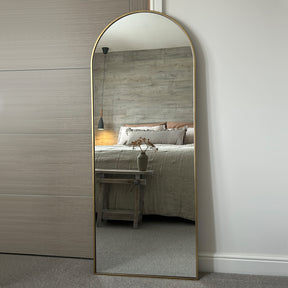 Full Length Gold Large Arched Metal Mirror leaning against wall in bedroom