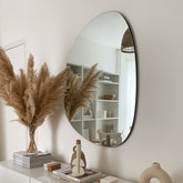 Large Frameless Pond Mirror above console table adorned with books and plants