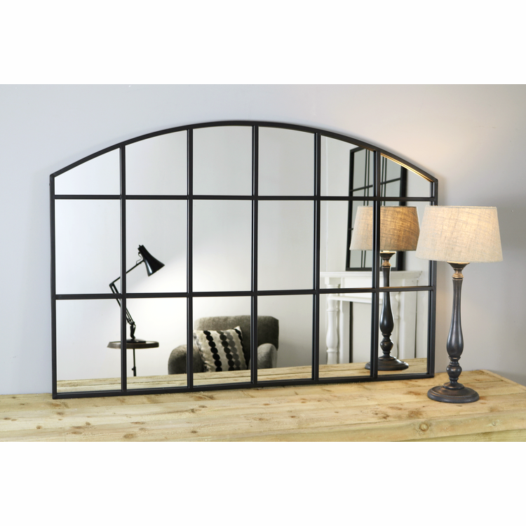 Black industrial arched metal window mirror displayed on wooden table