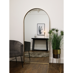 Full length arched gold large metal mirror leaning against wall